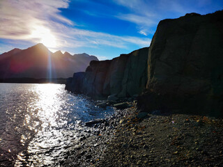 A striking Icelandic coastline with towering cliffs and the sun setting over calm waters, casting a...