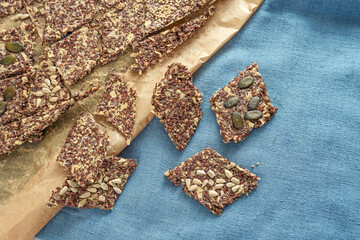Crunchy whole grain snacks from oat and linseed topped with various seeds on baking paper and a blue napkin, healthy baking, top view from above, copy space
