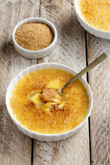 Traditional french portioned dessert creme brulee with creme, sugar and egg yolks. Burnt caramel crust. White ramekin on a old wooden table. Golden teaspoon with a creme brulee 