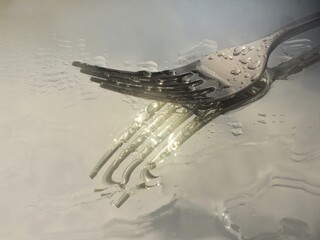 Close Up de tenedor de acero reflejado en un espejo con gotas de agua Imagen artística de tenedor...