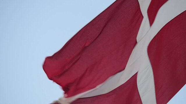 The flag of Denmark (Dannebrogen), waving calmly in the wind, while attached to a flagpole. It's recognized as the worlds oldest official flag.