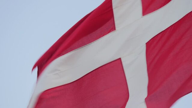 The flag of Denmark (Dannebrogen), waving calmly in the wind, while attached to a flagpole. It's recognized as the worlds oldest official flag.