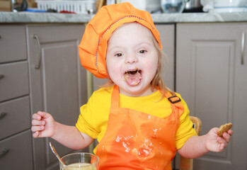 Portrait of a girl with Down syndrome. Child dressed as a chef. The girl is eating cookies. Joyful...