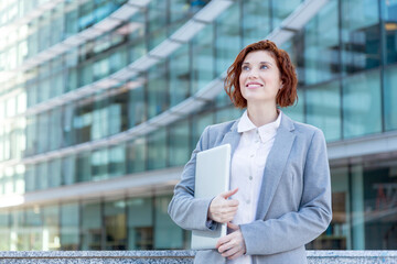 Happy executive woman holding laptop in office complex