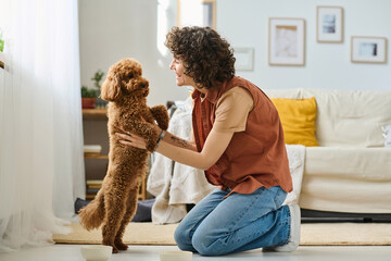 Young happy woman playing with her little dog in the room at home