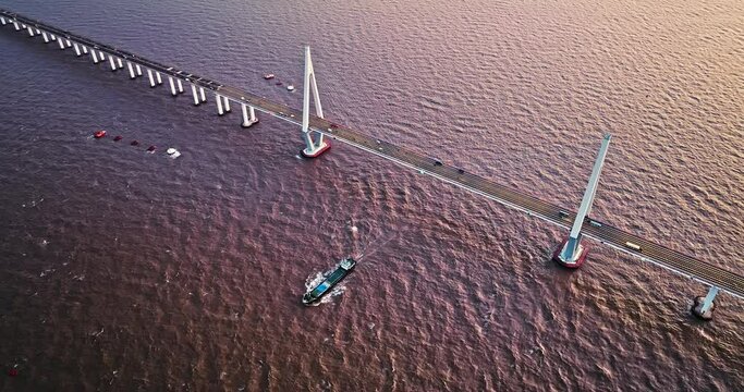 Aerial view of Hangzhou bay bridge scenery at sunset in Jiaxing, Zhejiang Province, China. A cargo ship passed under the bridge.