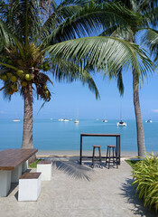 Table and chairs on the beach in Koh Samui, Thailand. Ocean landscape with boats as background. 
