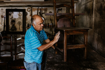 latin senior man carpenter working on wood chair at the furniture workshop in Mexico Latin America, hispanic people