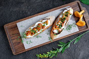 Two Bruschetta with chanterelles and Philadelphia cream cheese on a wooden board. Mushroom sandwich decorated with greens, top view