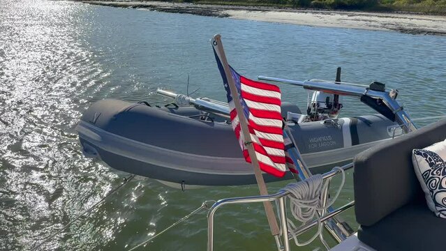 Close up view, rear of sailboat with dingy and American flag sailing on sunny day