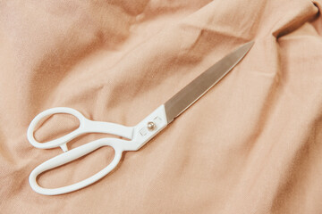 Steel tailor scissors on beige natural fabric. For seamstresses, making clothes, accessories, handicrafts, close up