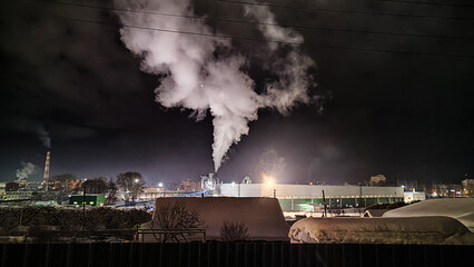 Night industrial landscape. View of a large plant and snow-covered territory. Cold winter weather....