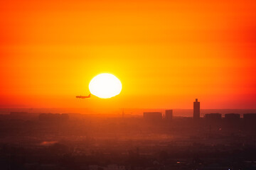 the plane landing and the sun behind it with the cityscape on the background