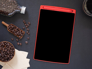 Naklejka premium Top view, flat lay tablet pc and scoop of coffee beans, bottle, bowl on on black table leather. Concept for cafe menu..