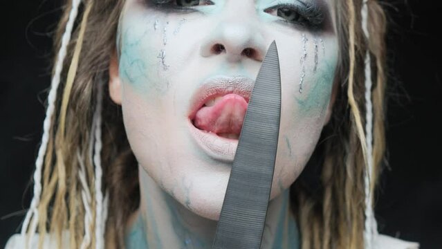 Dangerous woman licking a knife with blood close-up. Halloween or horror theme.