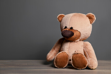 Cute teddy bear on wooden table near black wall, space for text