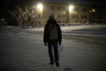 Man walks at night with backpack on street. Guy walking in snow. Details of hike at night.