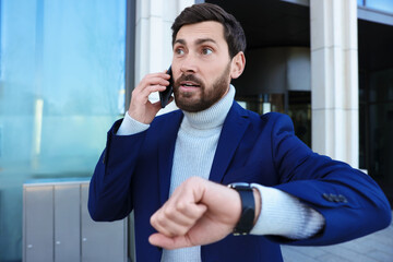 Emotional businessman talking on smartphone near building. Being late concept