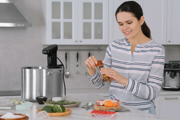 Woman grinding pepper onto meat near pot with sous vide cooker in kitchen. Thermal immersion...