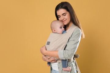 Mother holding her child in sling (baby carrier) on beige background. Space for text