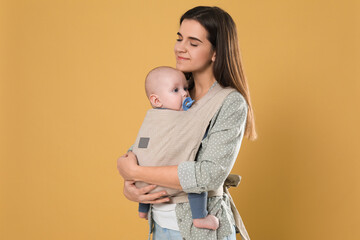 Mother holding her child in sling (baby carrier) on beige background