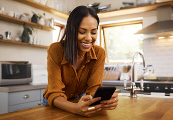 Happy woman, phone text and kitchen in a home reading a web app. House, female and smile of a young person with joy resting on a counter top table feeling relax typing with mobile networking - obrazy, fototapety, plakaty