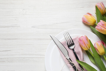 Stylish table setting with cutlery and tulips on white wooden background, flat lay. Space for text