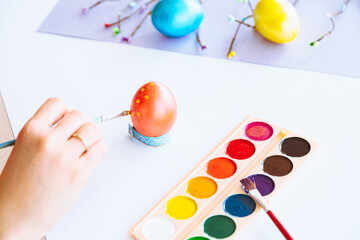 Woman hand painting easter egg with watercolors, preparation for egg hunt game. Happy easter congratulation symbol.