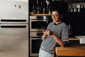 African woman using mobile phone while standing in kitchen