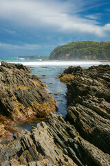 Rugged rocky foreshore with large waves beyond inlet in rock