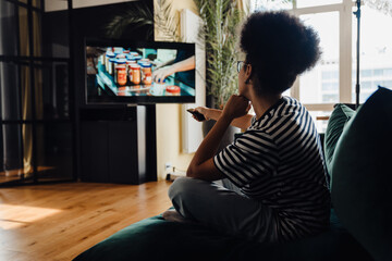 Back view of afro woman watching tv while sitting on couch
