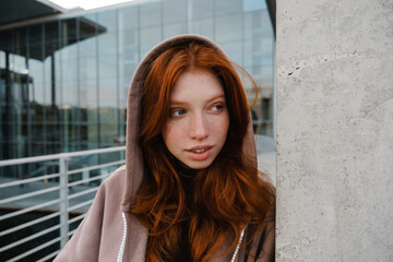 Fototapeta premium Redhead girl looking aside while standing outdoors
