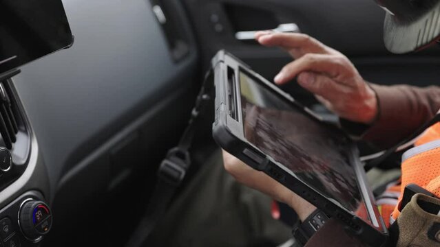 man working on a tablet inside the cab of a truck wearing ppe high viz vest and hard hat and another tablet visible in the corner