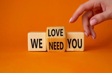 We love and need You symbol. Businessman Hand points at turned wooden cubes with words We need you and We love you. Beautiful orange background. Business and We love and need You concept. Copy space