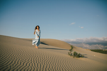 Fototapeta na wymiar Woman with long hair in a stylish dress poses in the desert sands.