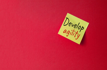 Develop agility symbol. Orange steaky note with concept words Develop Agility. Beautiful red background. Business and Develop agility concept. Copy space