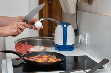 Cooking scrambled eggs with ham. Breaking an egg