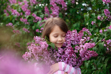 Fototapeta premium a little girl in a lilac bush, a girl near a flowering bush, lilacs in spring, bushes bloom