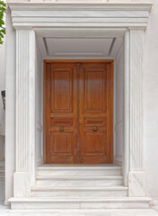 A simple, yet luxury house entrance with a solid wood door and white marble decorated walls. Travel to Athens, Greece.