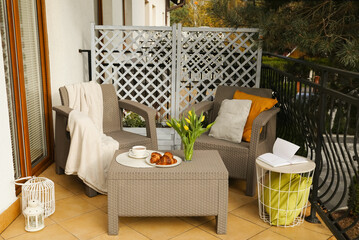 Different pillows, blanket, breakfast and tulips on rattan garden furniture outdoors