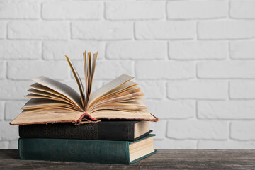 Stack of old hardcover books on wooden table near white brick wall, space for text