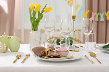 Festive Easter table setting with painted eggs, burning candles and yellow tulips indoors
