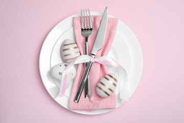 Festive table setting with painted eggs and cutlery on pink background, top view. Easter celebration