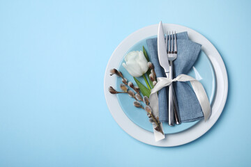 Festive table setting with willow twigs and tulip on light blue background, top view with space for text. Easter celebration