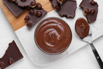 Bowl with tasty paste, spoon and pieces of chocolate on white wooden table, flat lay