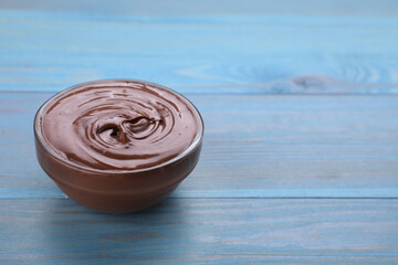 Bowl with tasty chocolate paste on light blue wooden table, closeup. Space for text