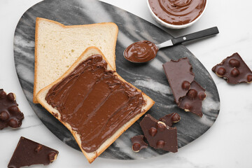 Tasty breakfast. Bread with sweet paste and chocolate served on white marble table, flat lay