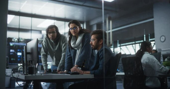 Group of Three Young Indian Software Engineers Use Computer to Discuss a Technological Project in Modern Industrial Office. Group of Male and Female Scientists Work in Research and Development Center