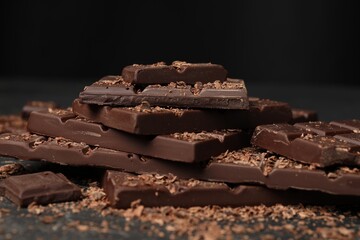 Pieces and shavings of tasty chocolate on dark table, closeup
