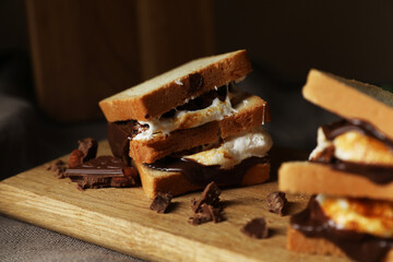 Delicious marshmallow sandwiches with bread and chocolate on wooden board, closeup